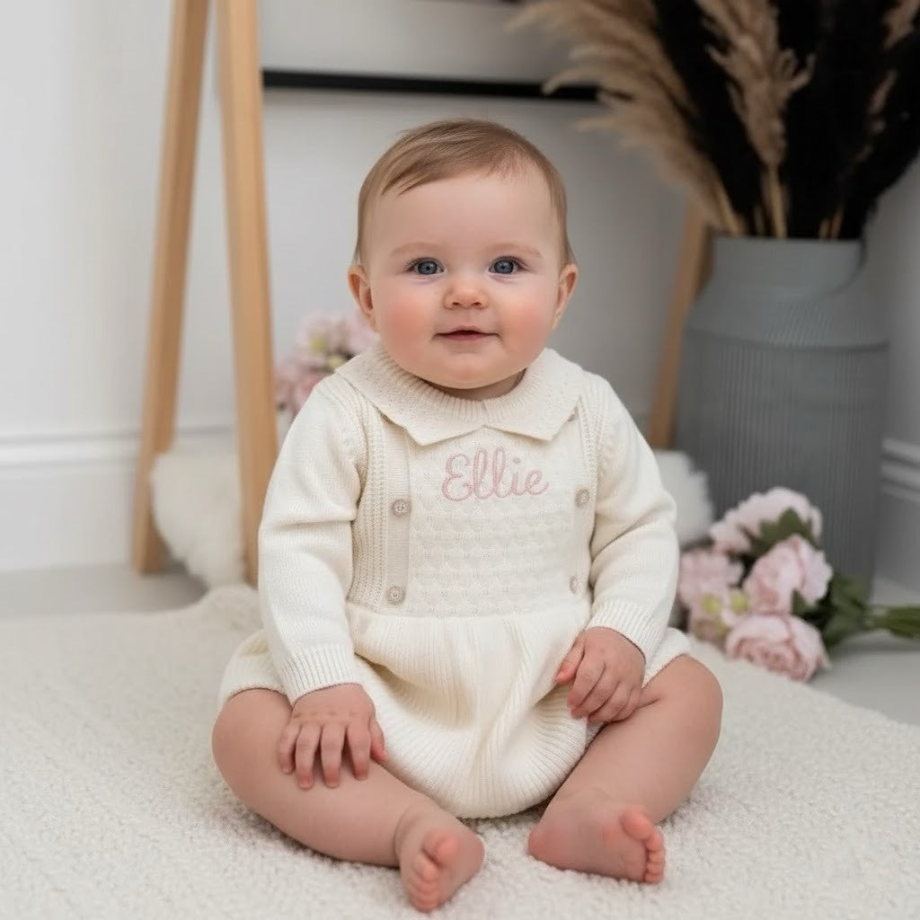 Baby wearing a white outfit with 'Ellie' embroidered on it, sitting on a white surface.