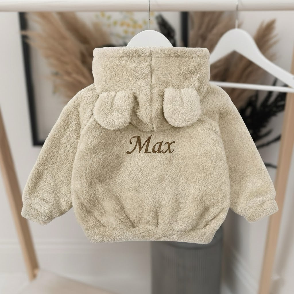 Beige children's jacket with 'Max' embroidered on it, hanging against a neutral background.