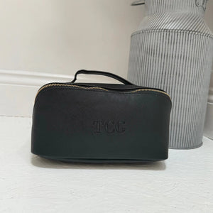 Black cosmetic bag with 'TCG' branding on a light surface.