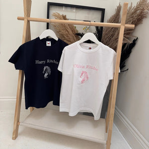 Two t-shirts, one navy and one white, with embroidered designs on a wooden rack.