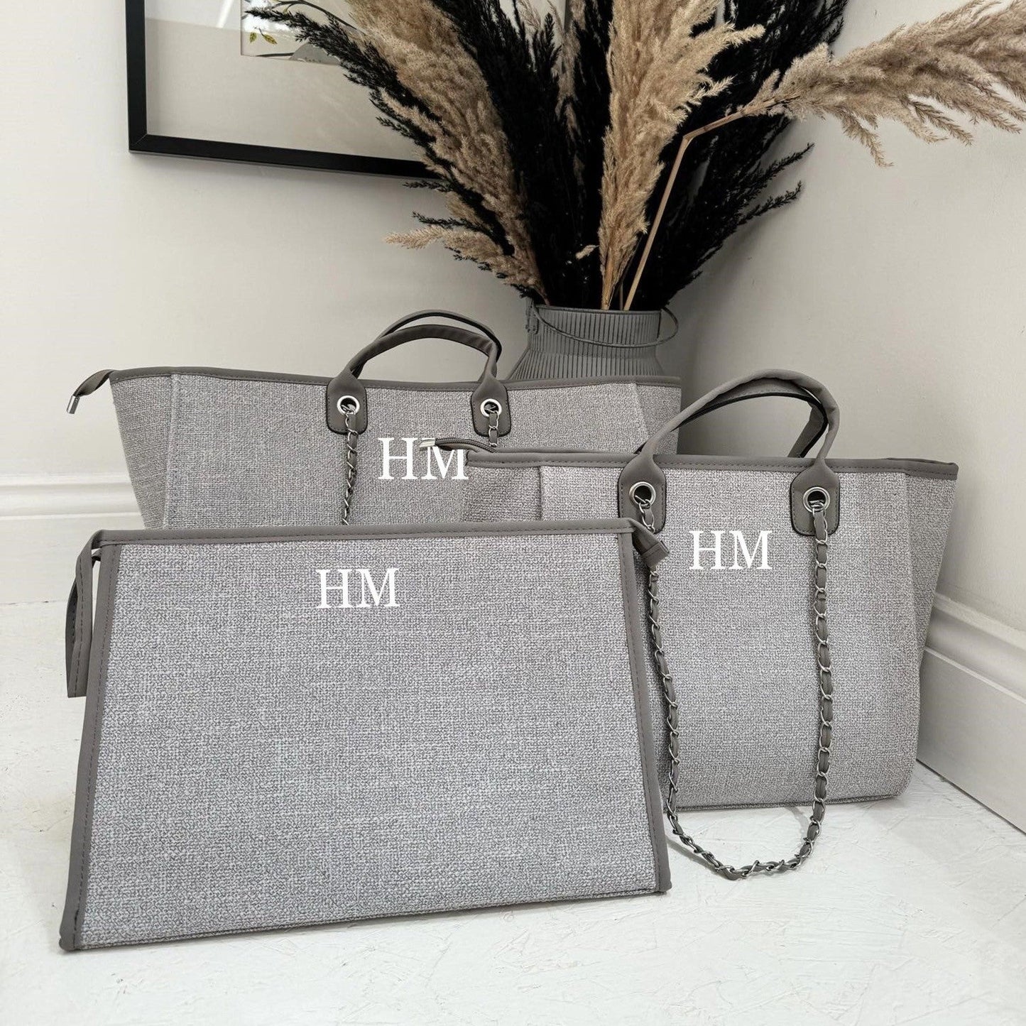 three grey custom tote bags and clutch bags with initials HM on them