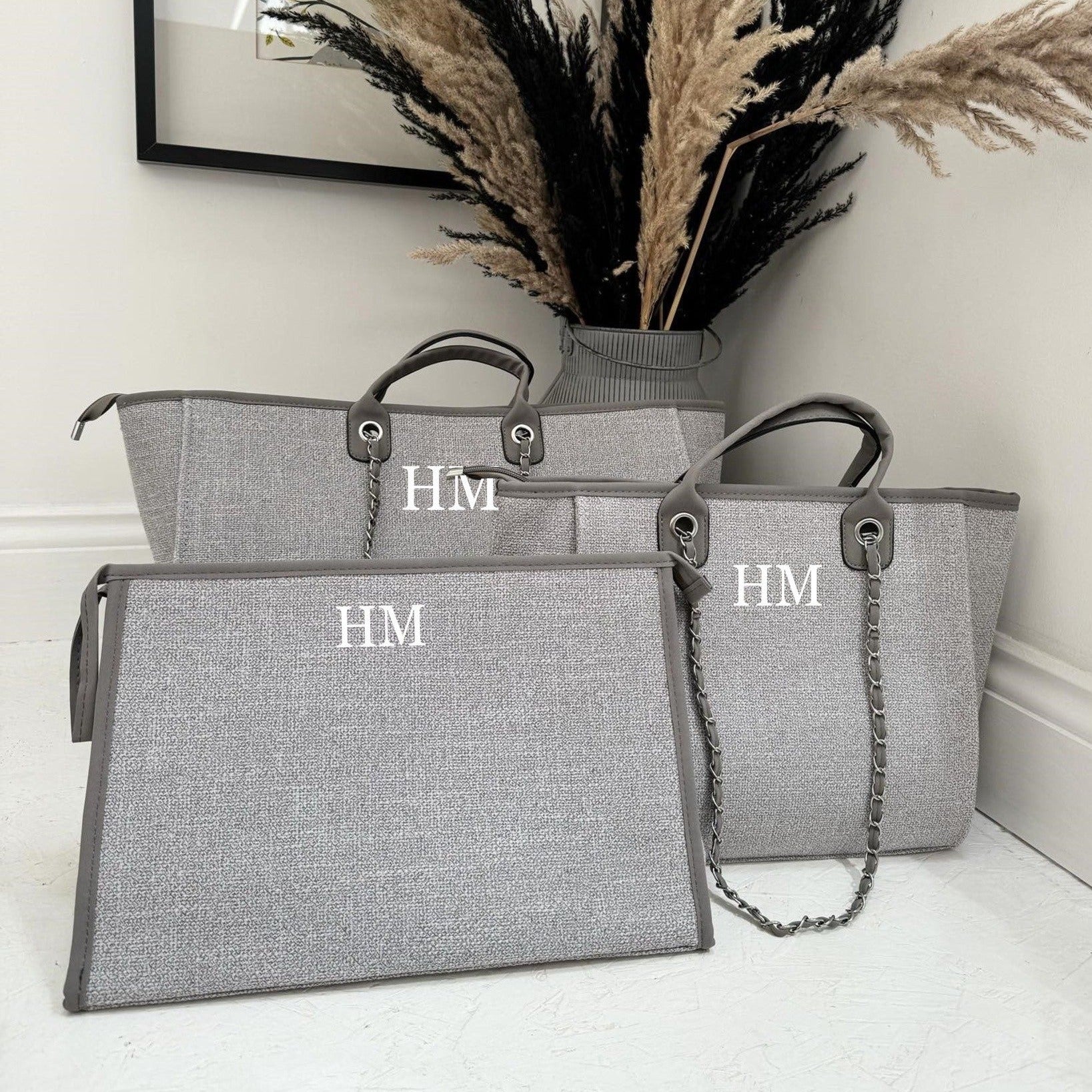 three grey custom tote bags and clutch bags with initials HM on them