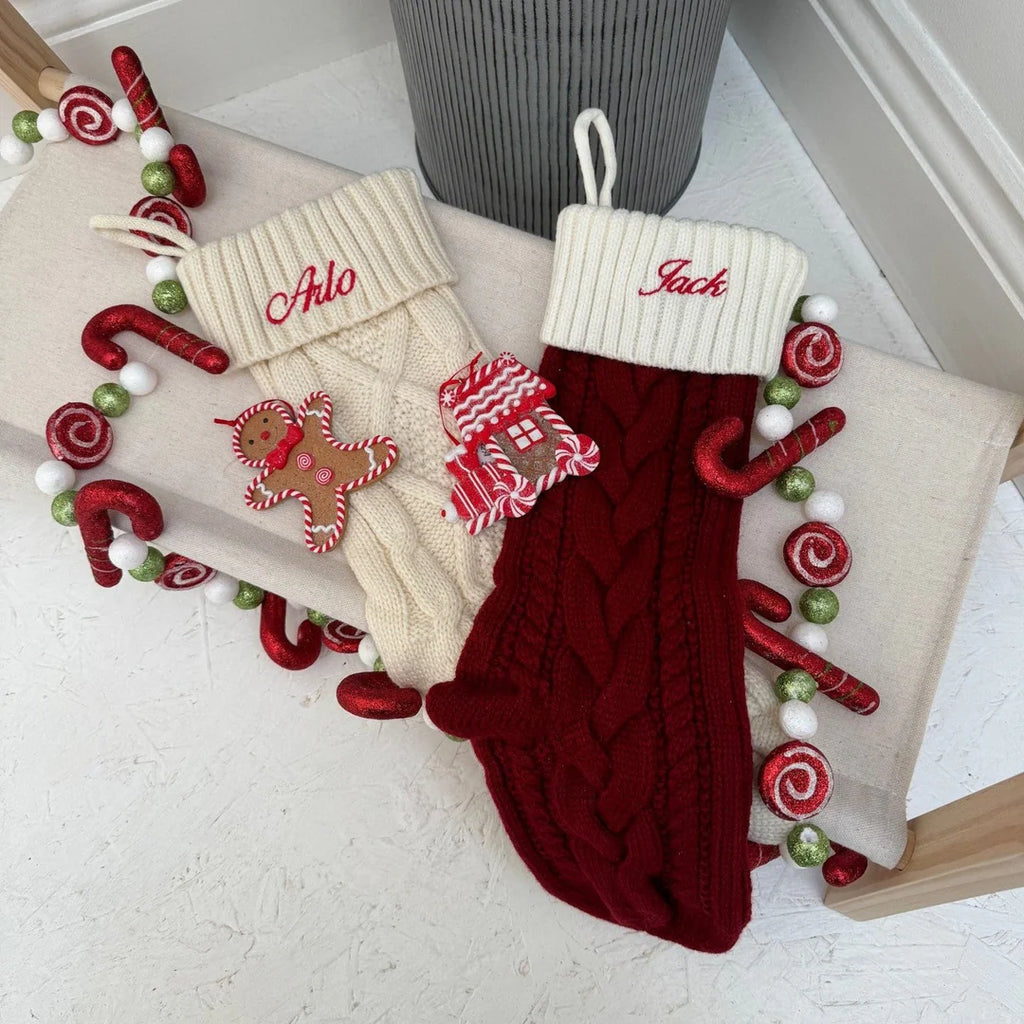 Two Christmas stockings, one red and one beige, with candy decorations on a white surface.
