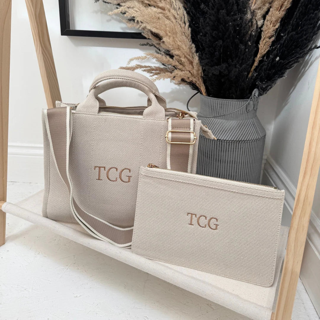 Beige handbag and pouch with 'TCG' monogram on a wooden shelf.