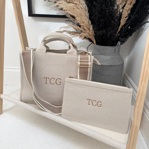 Beige handbag and pouch with 'TCG' monogram on a wooden shelf.