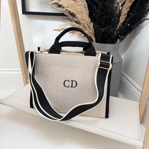 Beige tote bag with black straps and 'CD' monogram on a white surface.