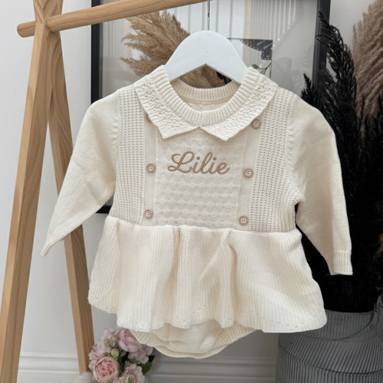White baby dress with 'Lilie' embroidery on a hanger against a neutral background