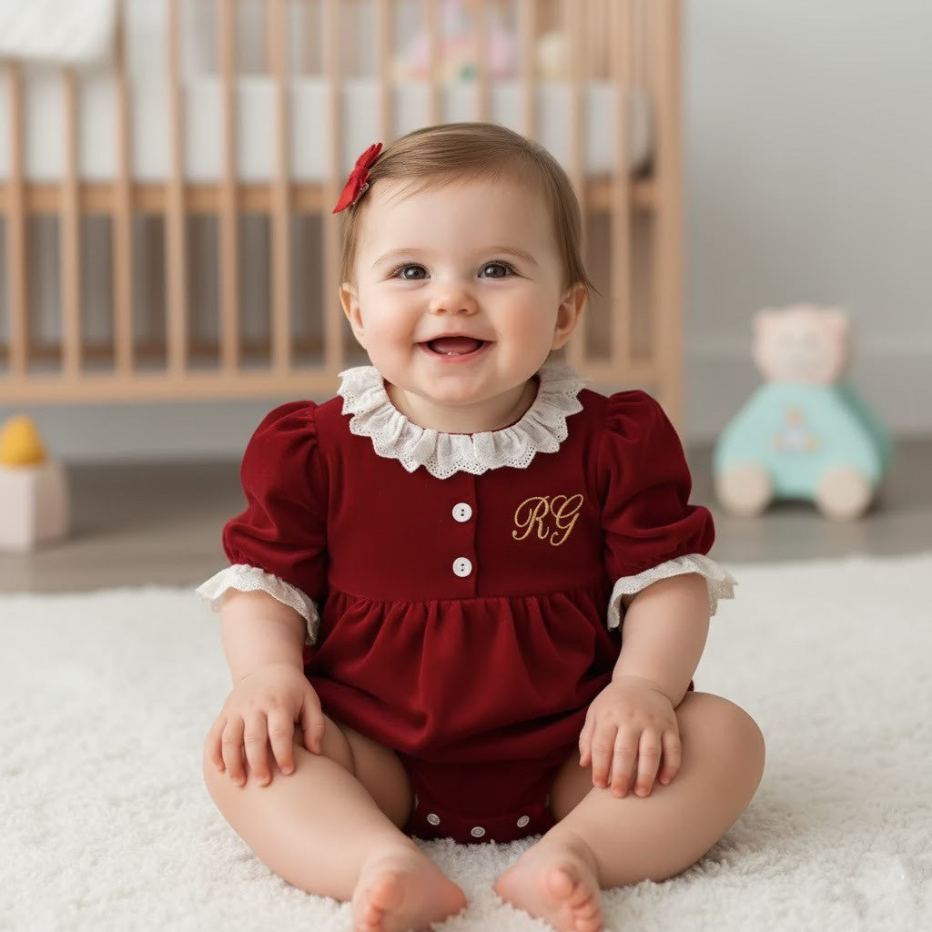 baby girl sat on the floor wearing a red romper with her initials on with a bow in her hair