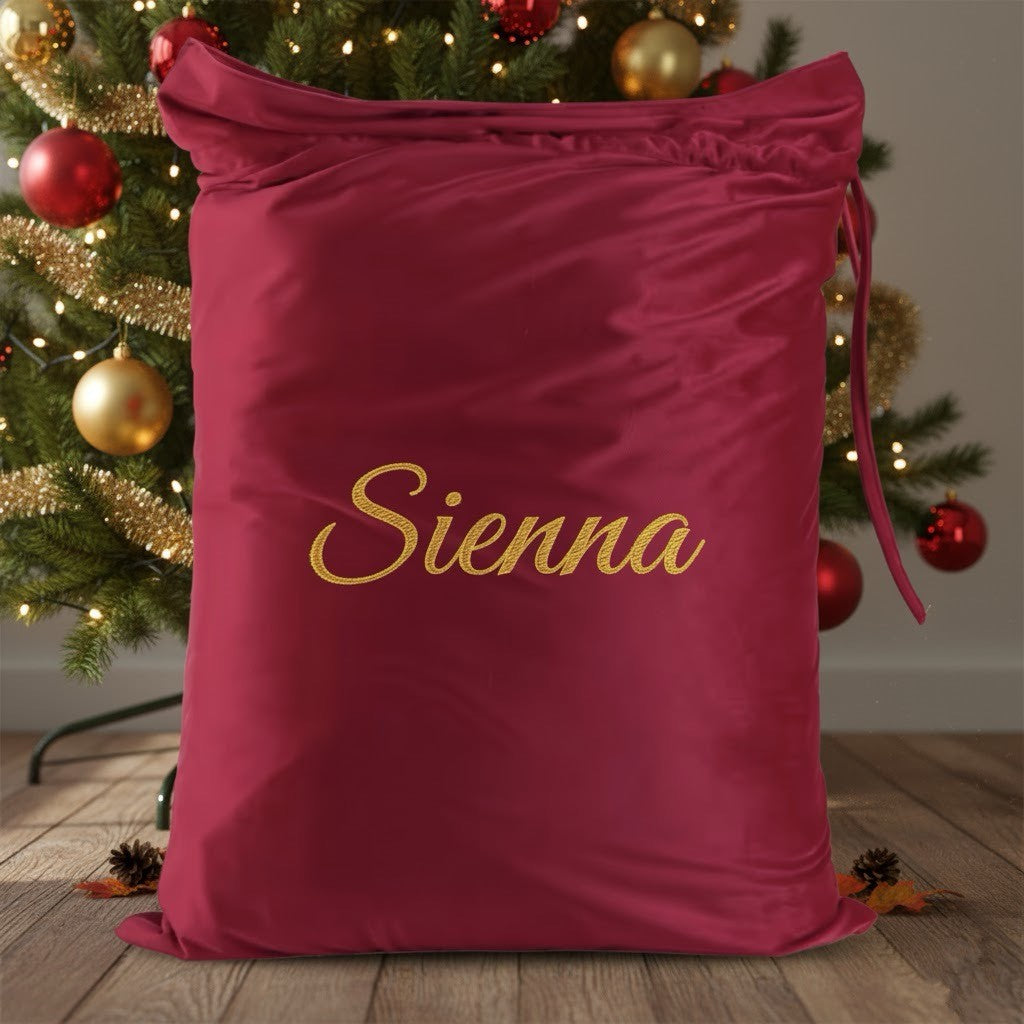 Red drawstring bag with 'Sienna' embroidered on it in front of a decorated Christmas tree.
