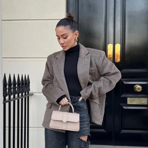 Woman in a gray coat holding a beige handbag in front of a black door. Personalised handbag