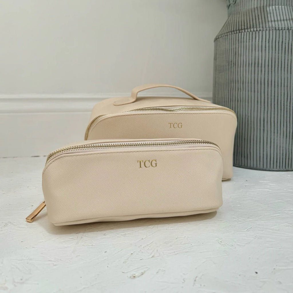 Beige toiletry bag with 'TCG' monogram on a light wooden surface.