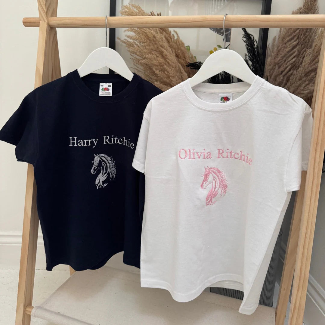 Two t-shirts with embroidered designs on hangers against a neutral background