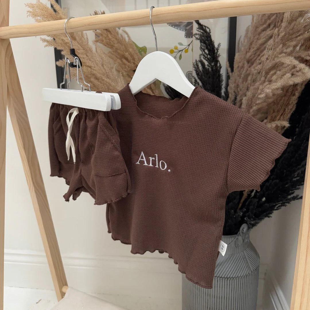 Brown children's outfit with 'Arlo' embroidery on a hanger against a neutral background.