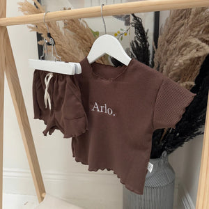 Brown children's outfit with 'Arlo' embroidery on a hanger against a neutral background.