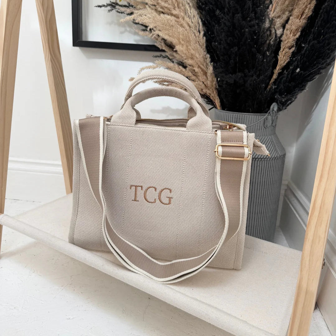 Beige handbag with 'TCG' monogram on a white surface, with dried plants in the background.