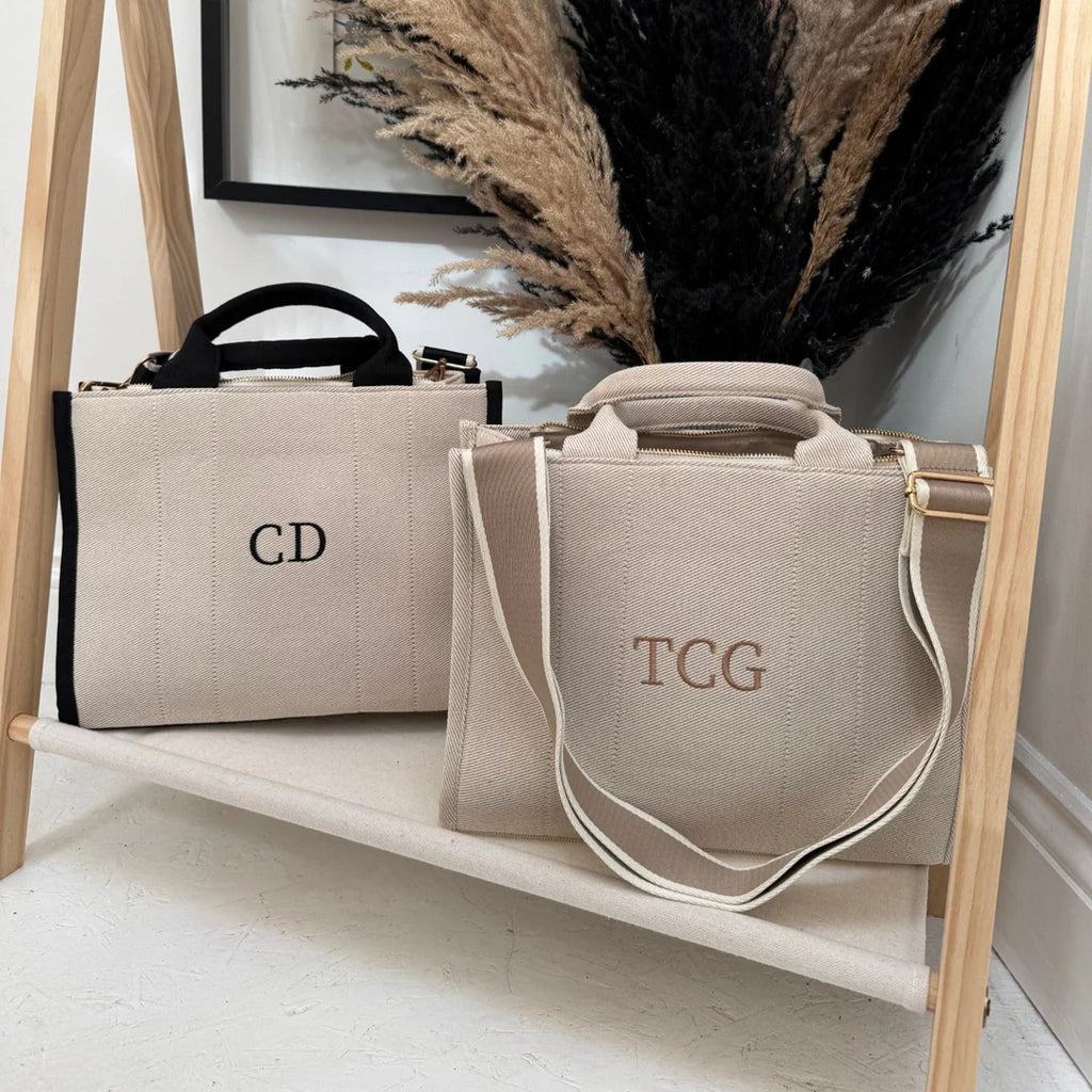 Two beige bags with monogrammed initials on a wooden shelf.