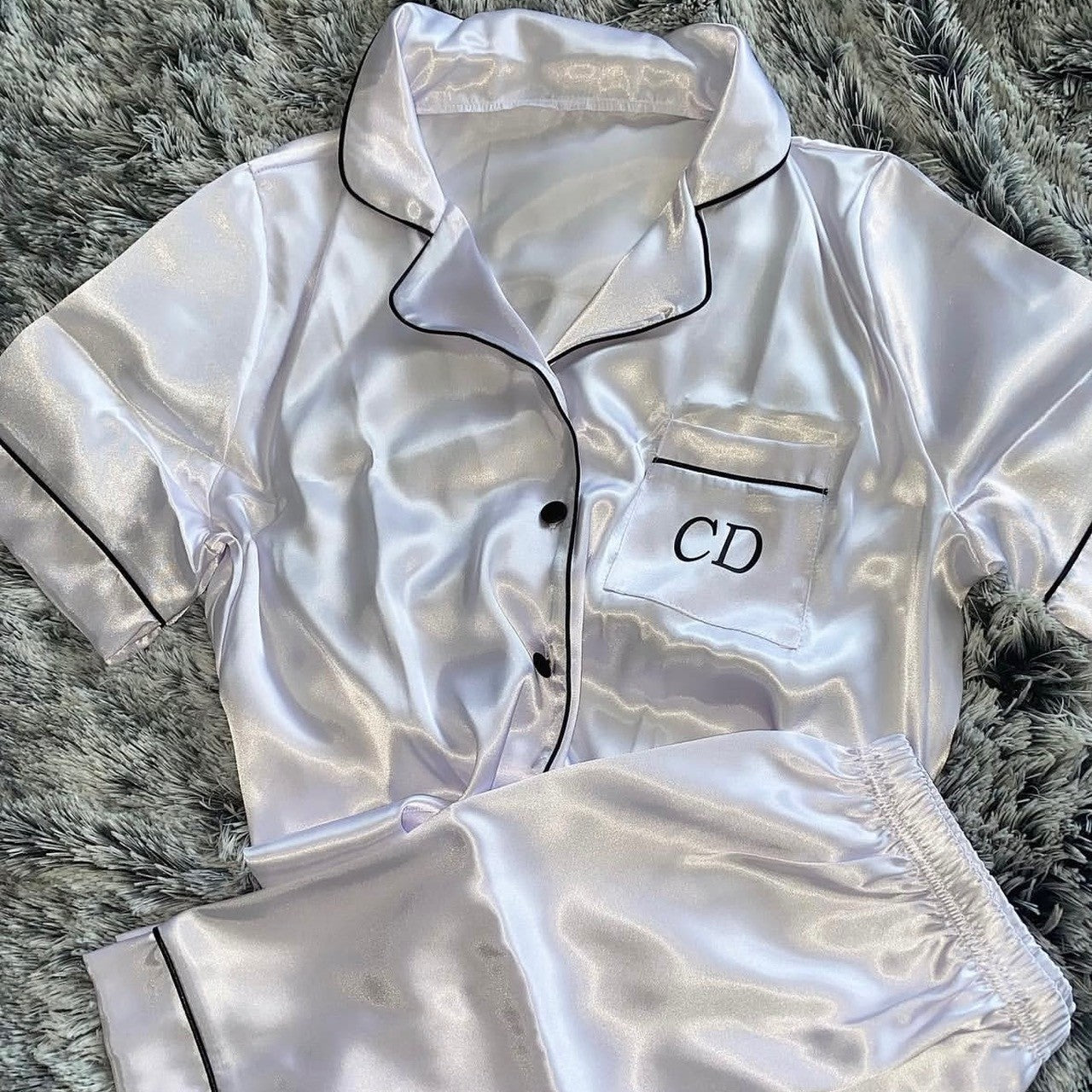 white satin pajama set with 'CD' monogram on a gray textured surface