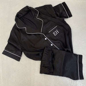 Black satin pajama set with white piping on a beige surface with EH initials 