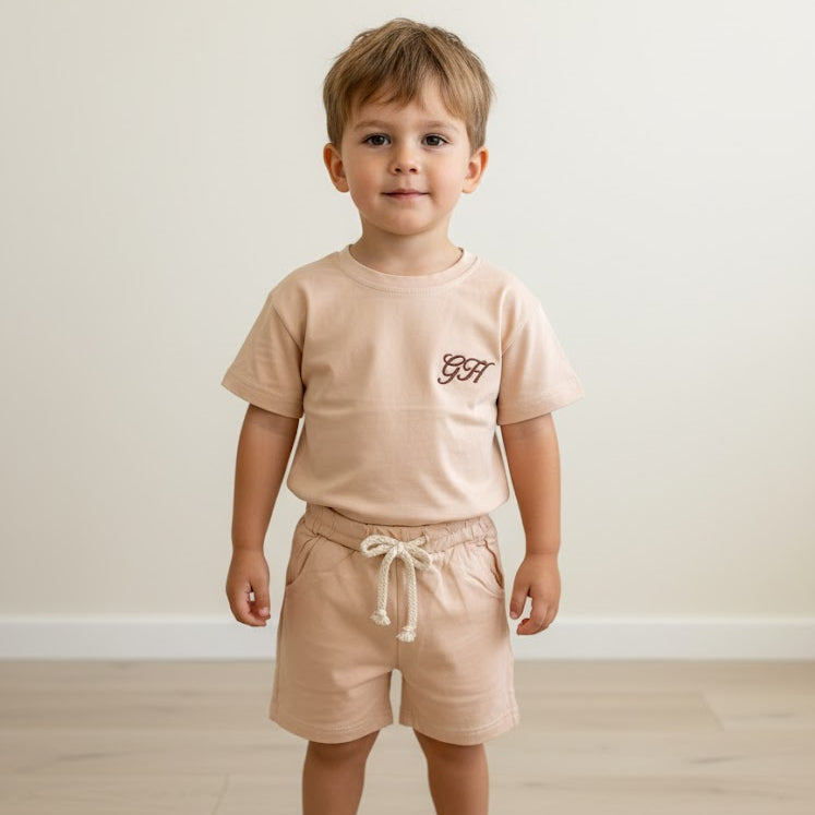 Child wearing a beige t-shirt and shorts set on a light wooden floor.