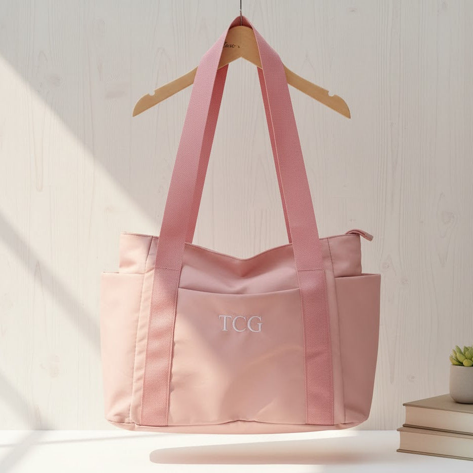 Pink tote bag with 'TCG' monogram on a white surface with a light background
