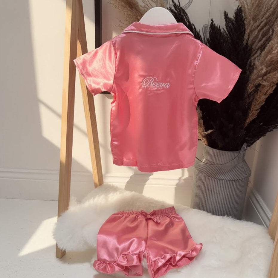 Pink satin outfit with 'Reeva' name on a mannequin against a neutral background.