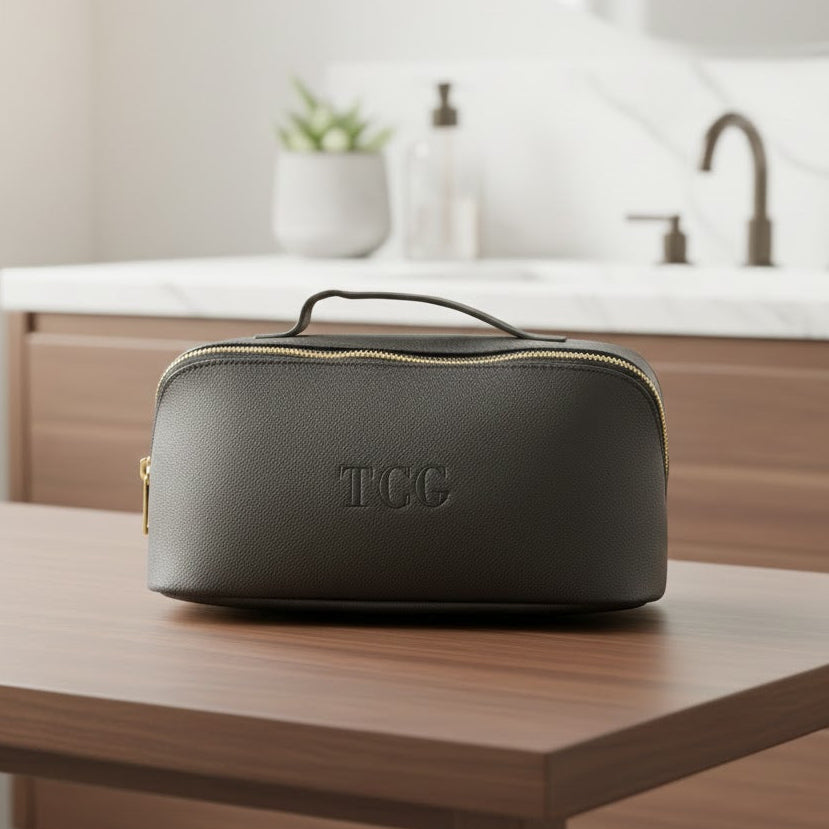 Black toiletry bag with 'TCC' initials on a wooden table in a bathroom setting