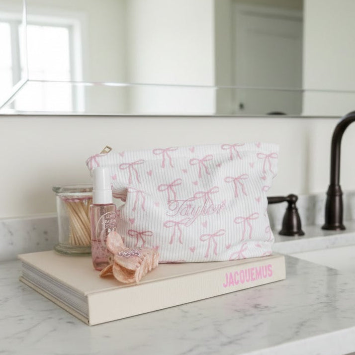 Bathroom counter with a white pouch, bottle, and book in front of a mirror.