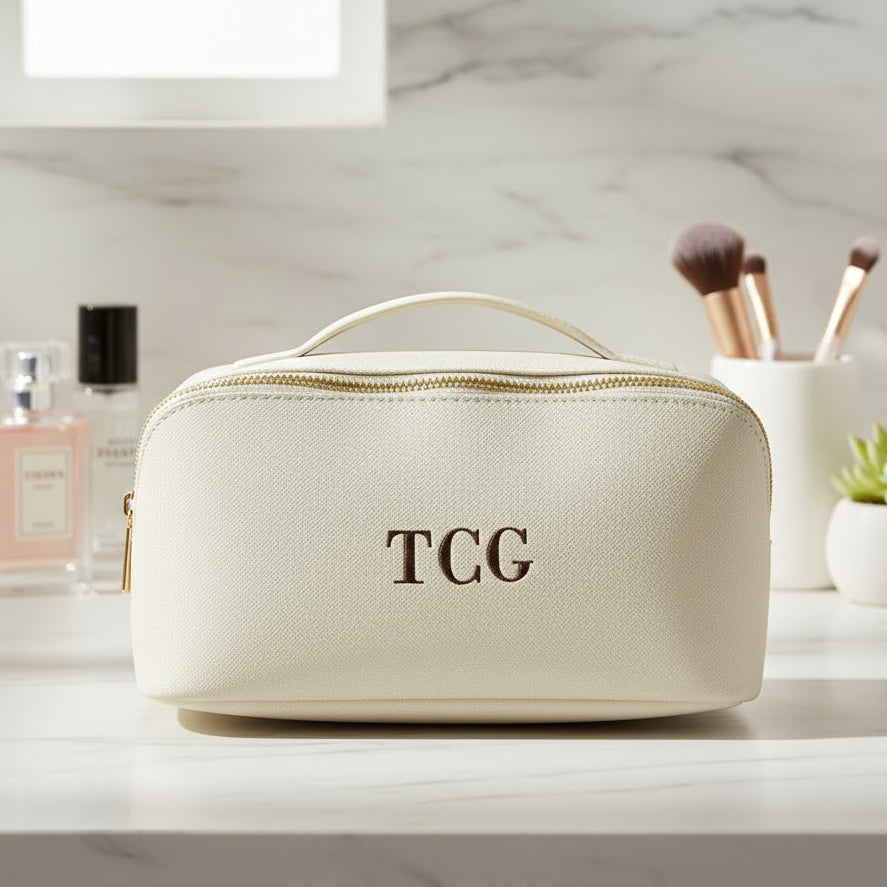 Beige toiletry bag with 'TCG' monogram on a marble surface with cosmetic items.
